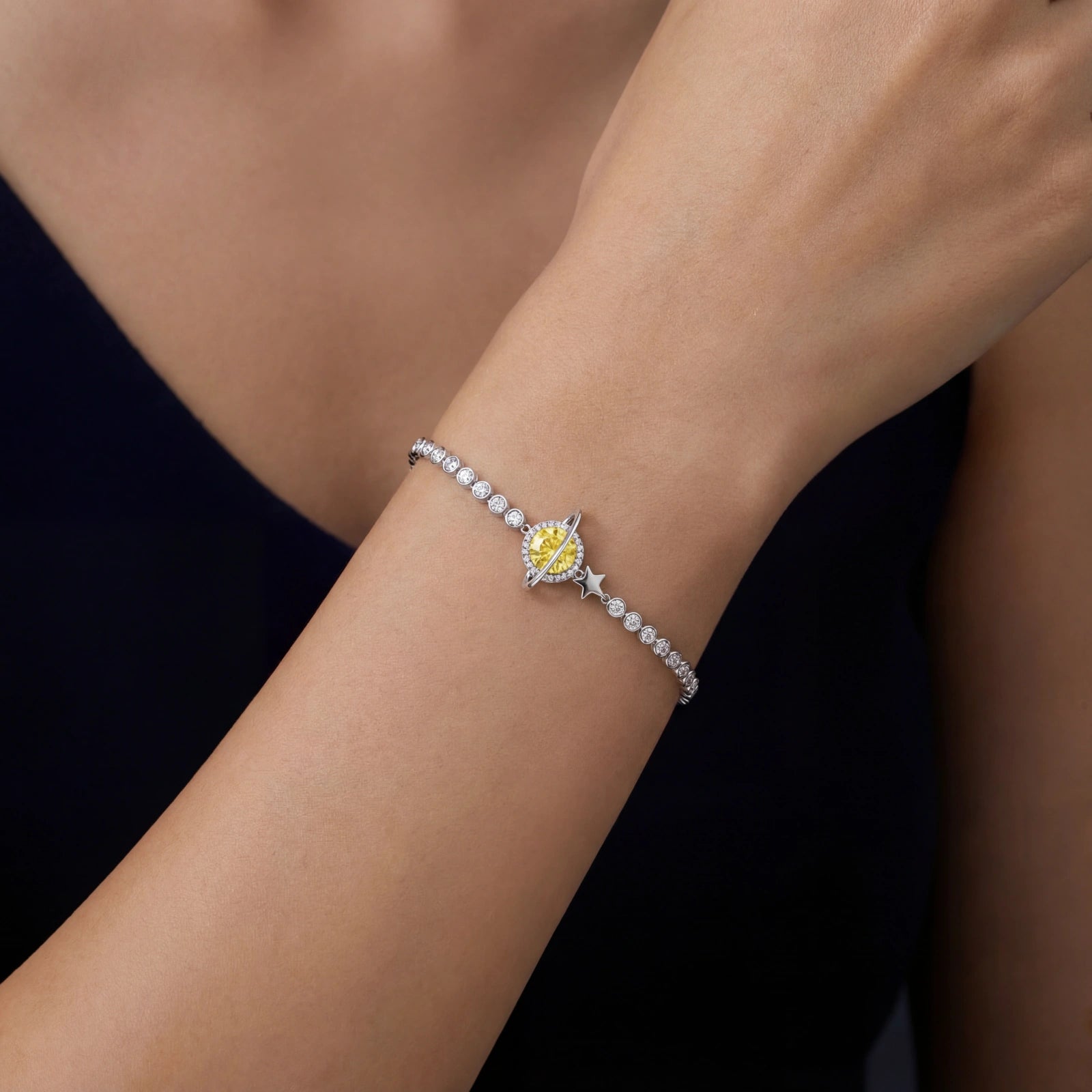 Silver bracelet with a yellow gemstone on a person's wrist against a dark background