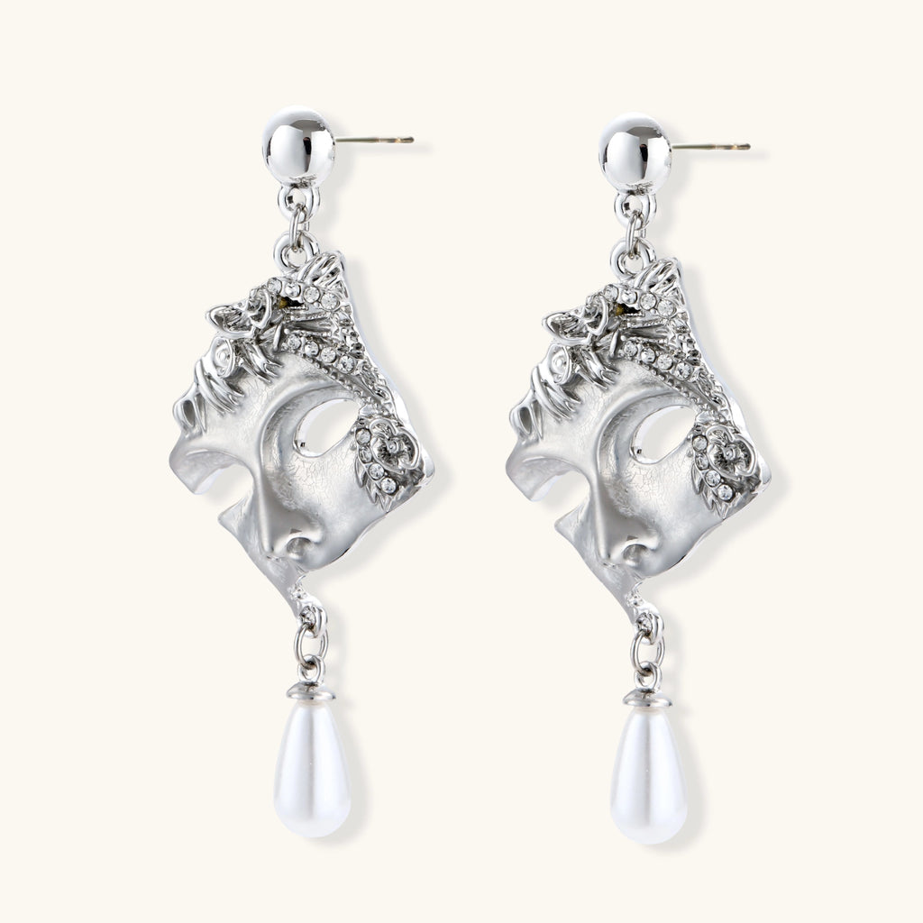 Pair of silver earrings with face designs and teardrop-shaped elements on a white background