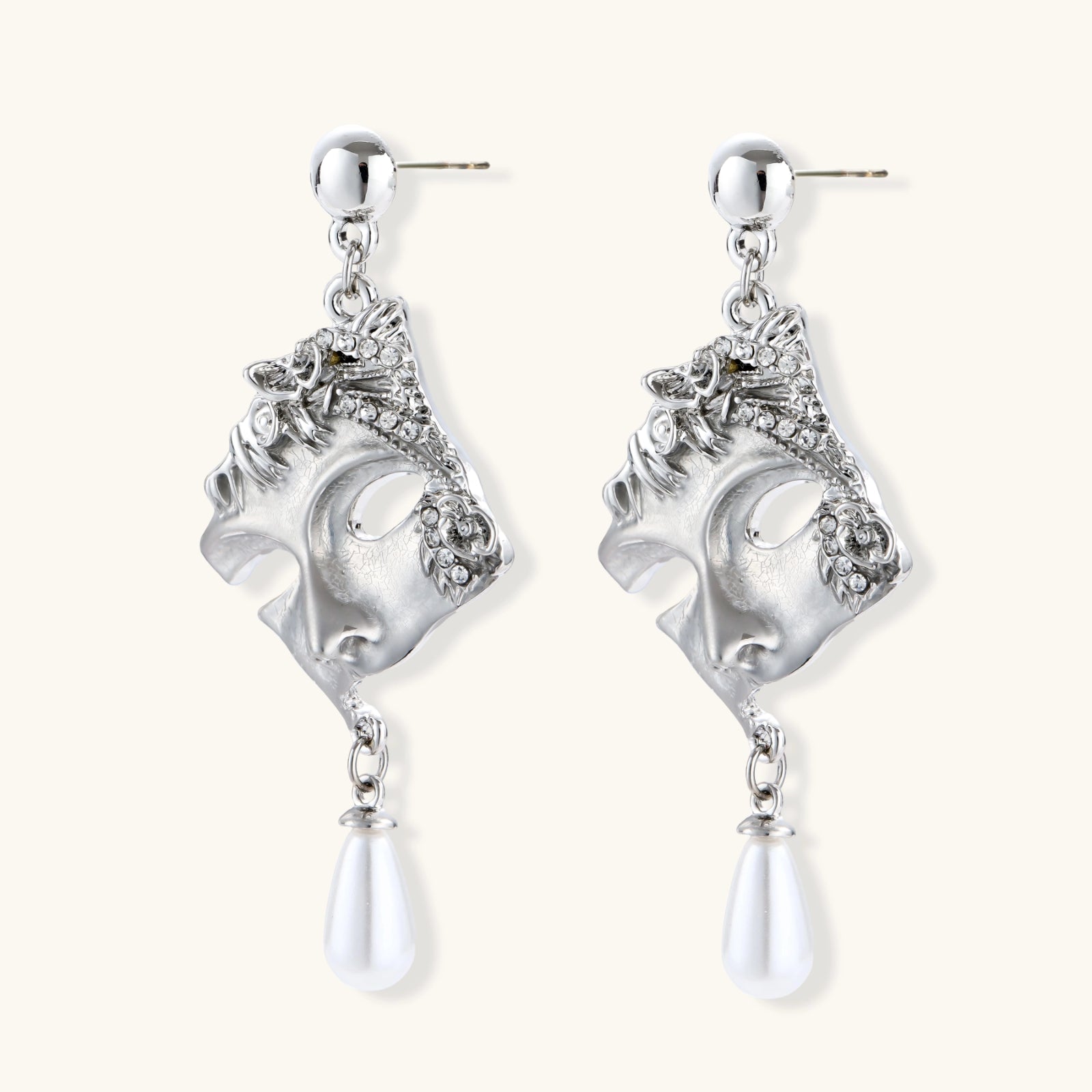 Pair of silver earrings with face designs and teardrop-shaped elements on a white background