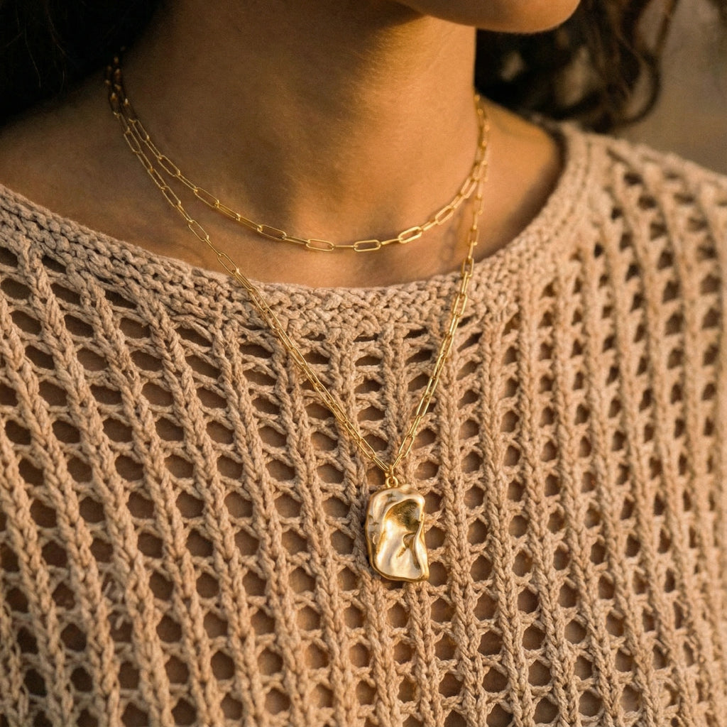 Close-up of a person wearing two gold necklaces on a beige textured garment.