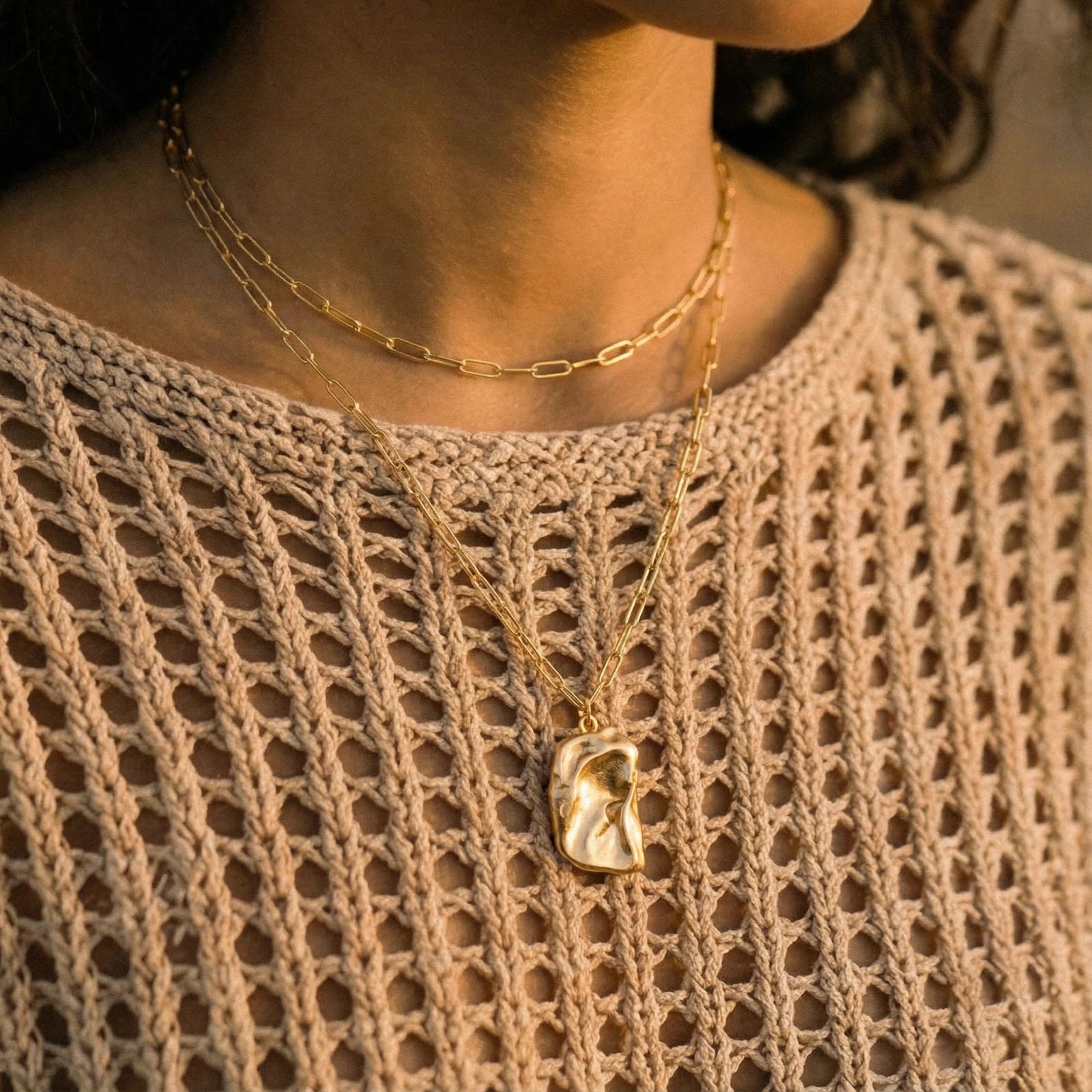 Close-up of a person wearing two gold necklaces on a beige textured garment.