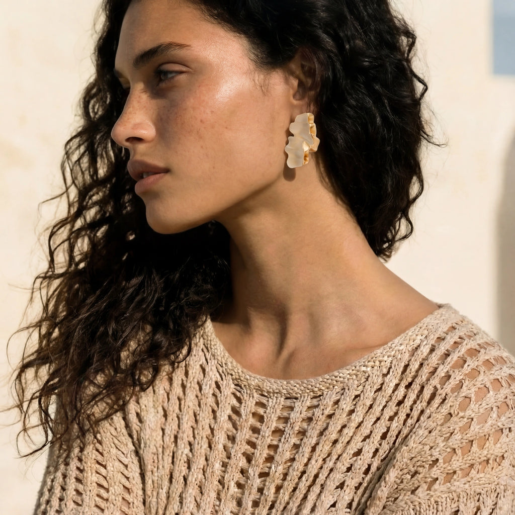 Woman wearing a beige knitted sweater and gold earrings against a neutral background
