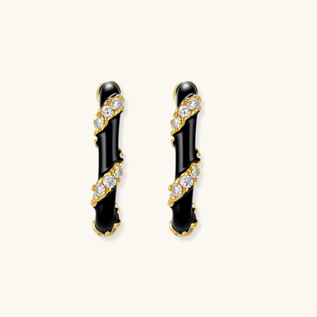 Pair of black and gold earrings with clear gemstones on a white background