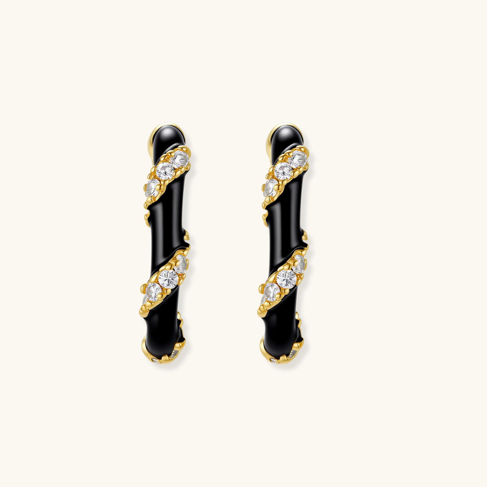 Pair of black and gold earrings with clear gemstones on a white background