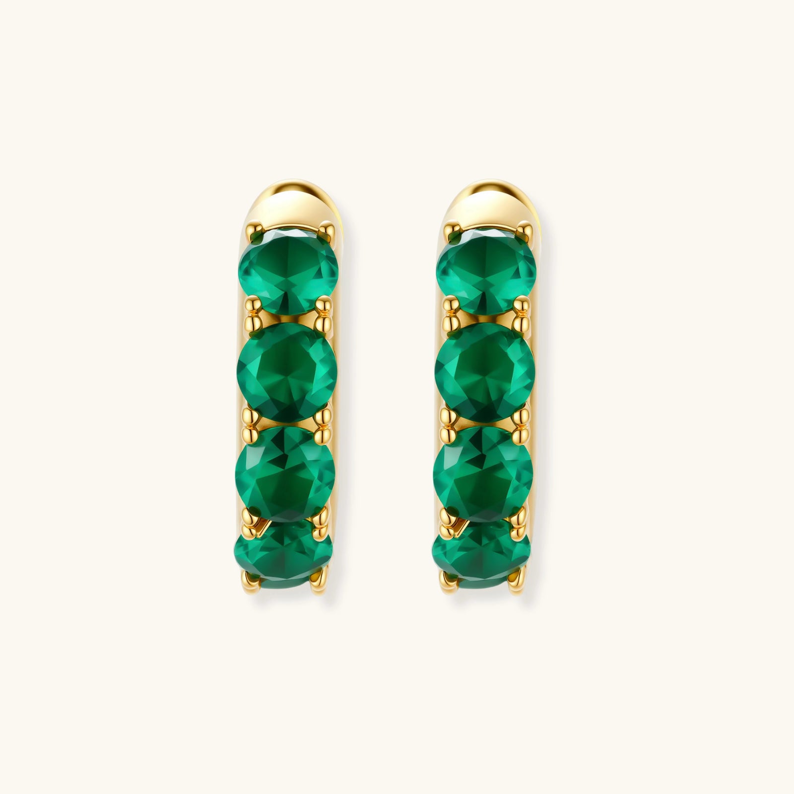 Gold hoop earrings with green gemstones on a white background