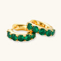 Gold hoop earrings with green gemstones on a white background