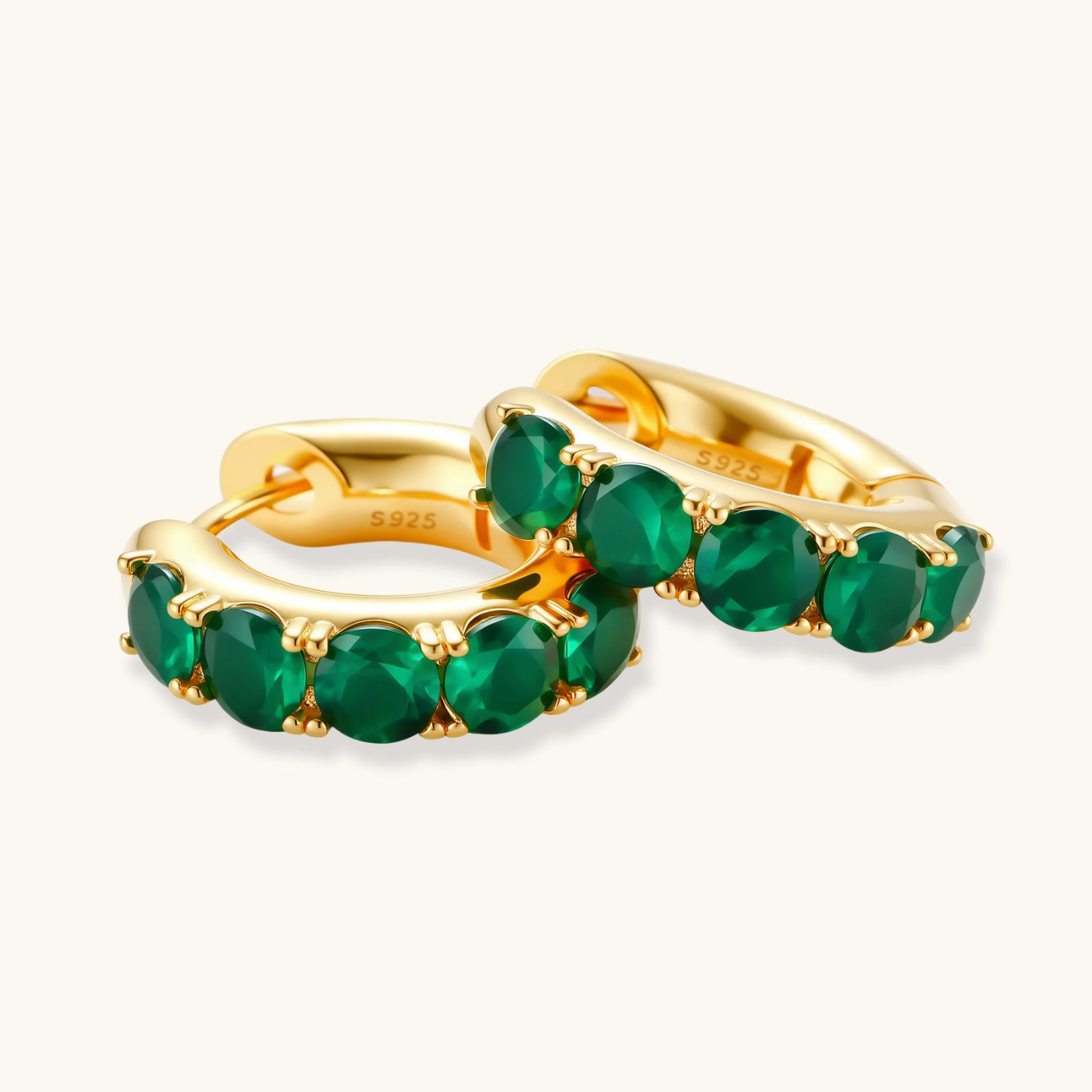 Gold hoop earrings with green gemstones on a white background