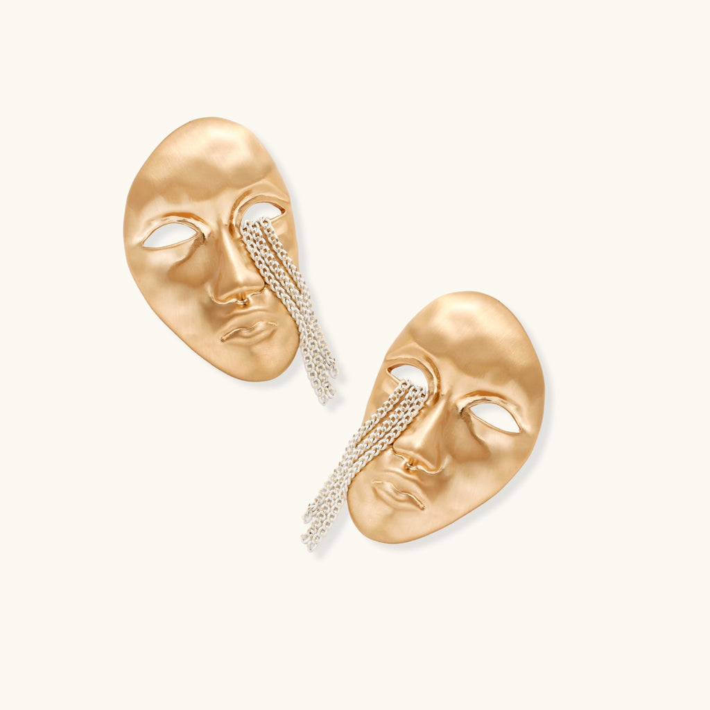 Gold mask-shaped earrings with chain details on a white background