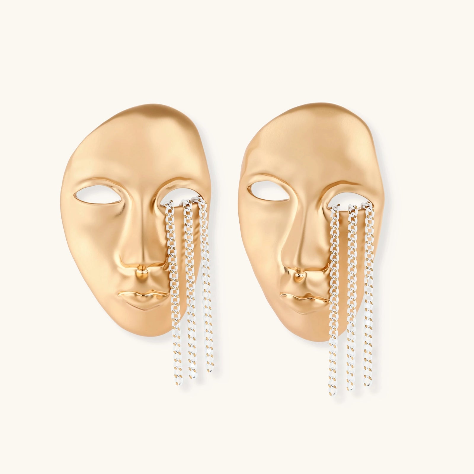 Gold mask-shaped earrings with chain details on a white background