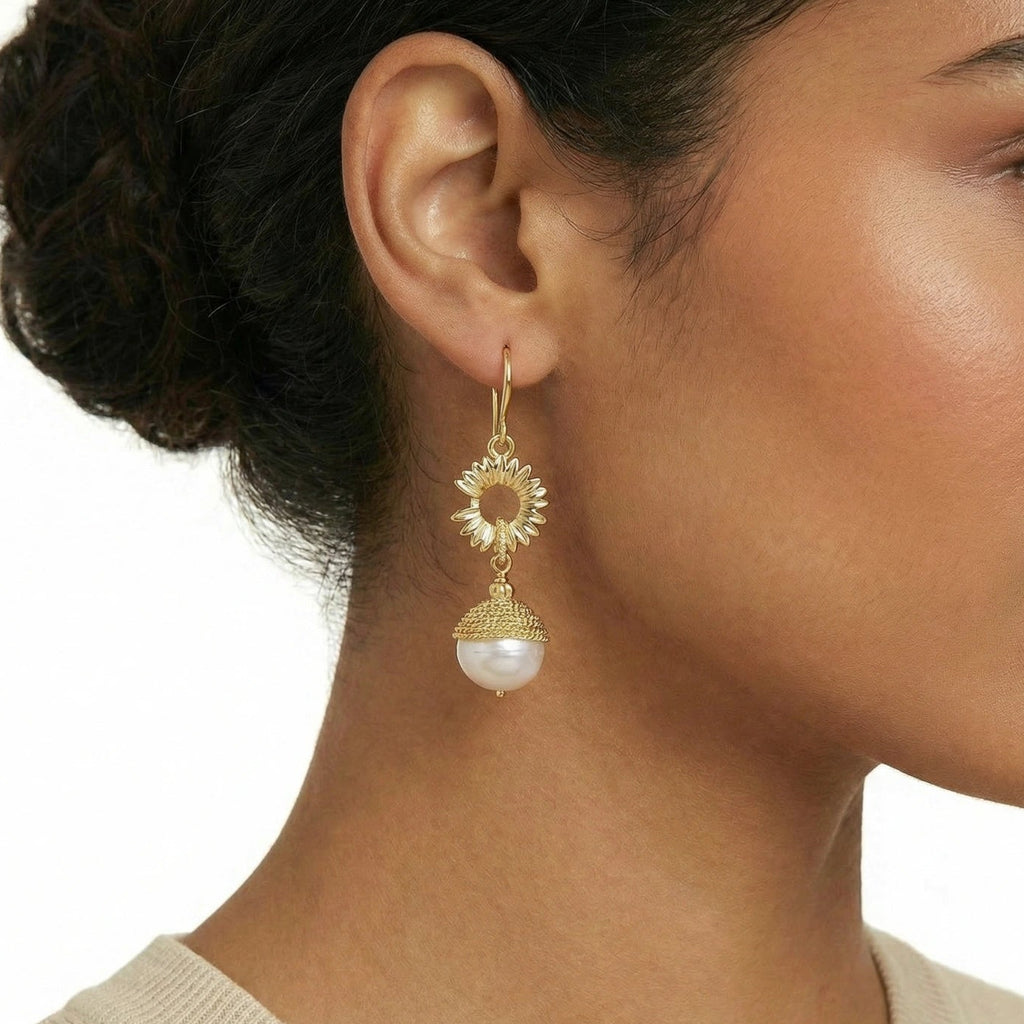 Close-up of a woman wearing a gold earring with a pearl drop on a neutral background