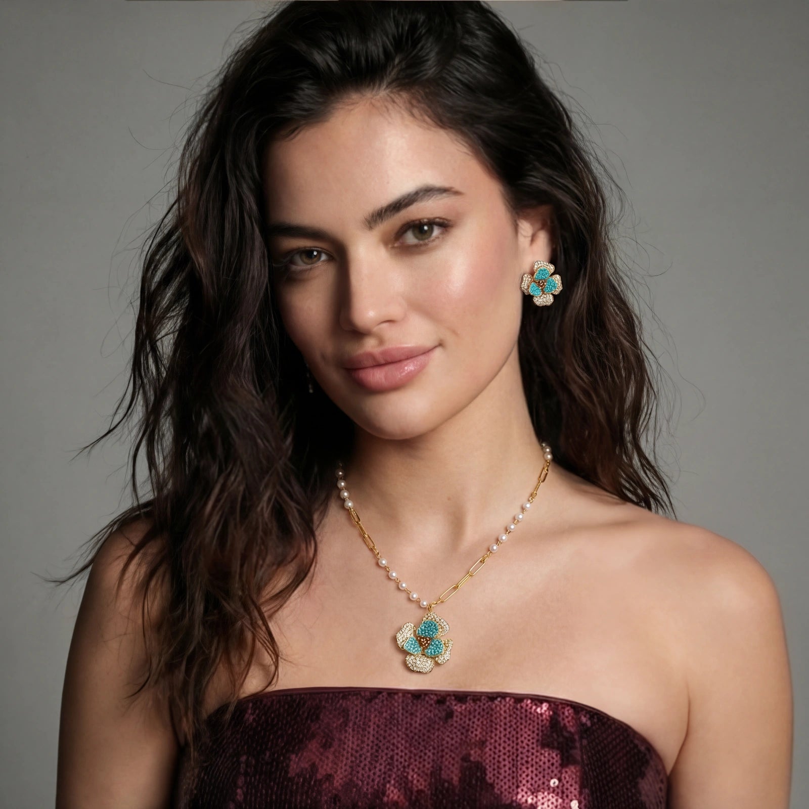 Woman wearing a rhinestone and turquoise floral necklace and earrings against a gray background