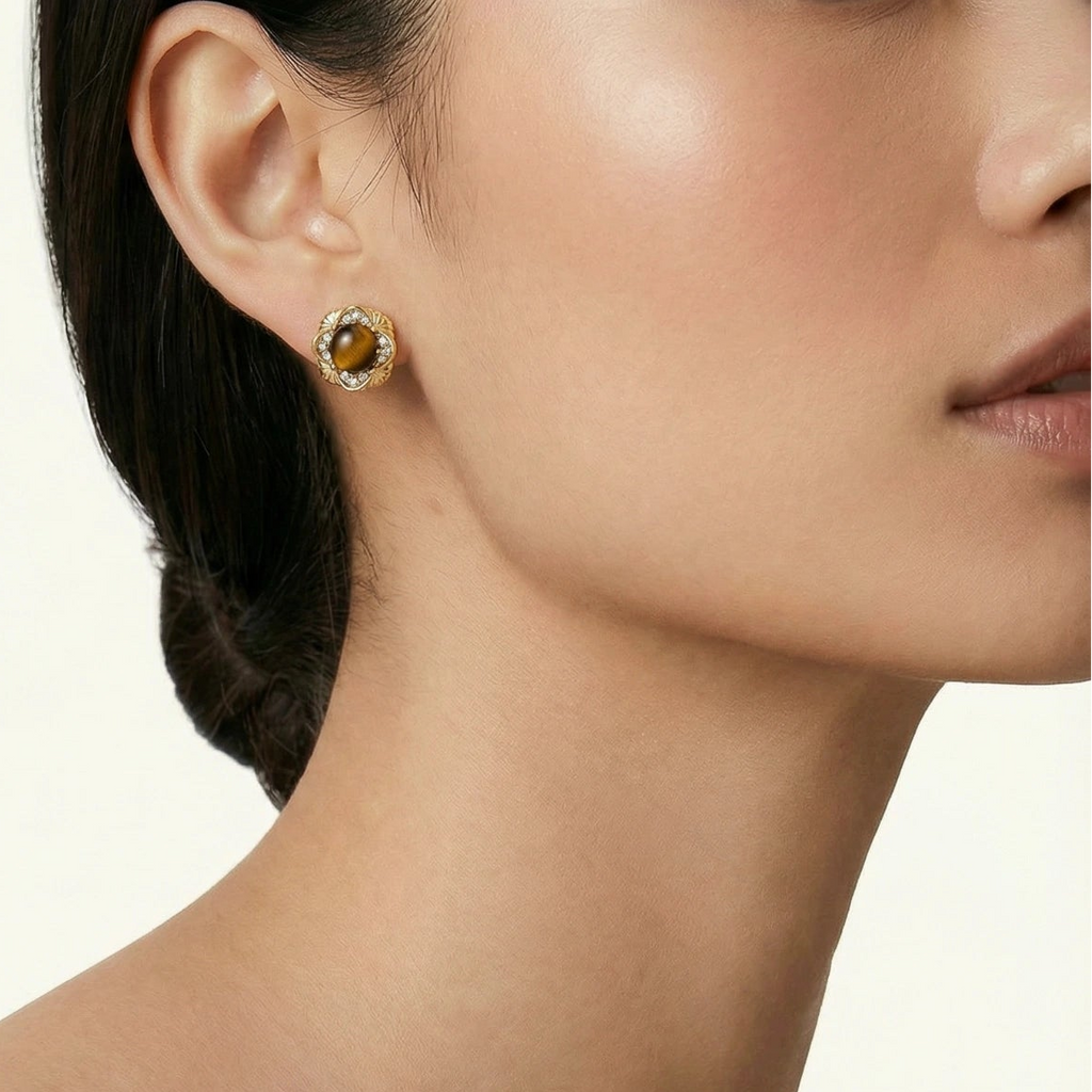 Close-up of a woman wearing a gold earring with a gemstone on a neutral background