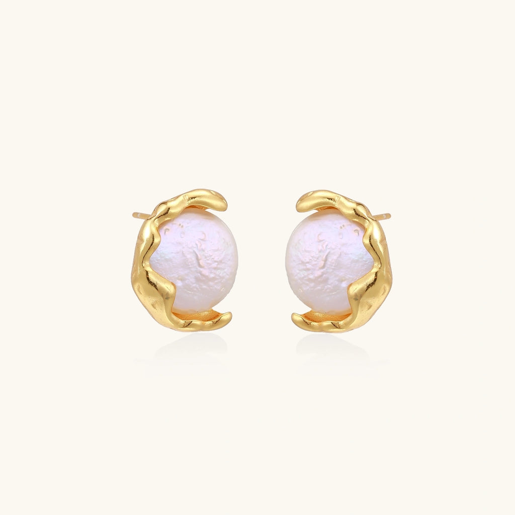 Gold earrings with pearls on a light beige background