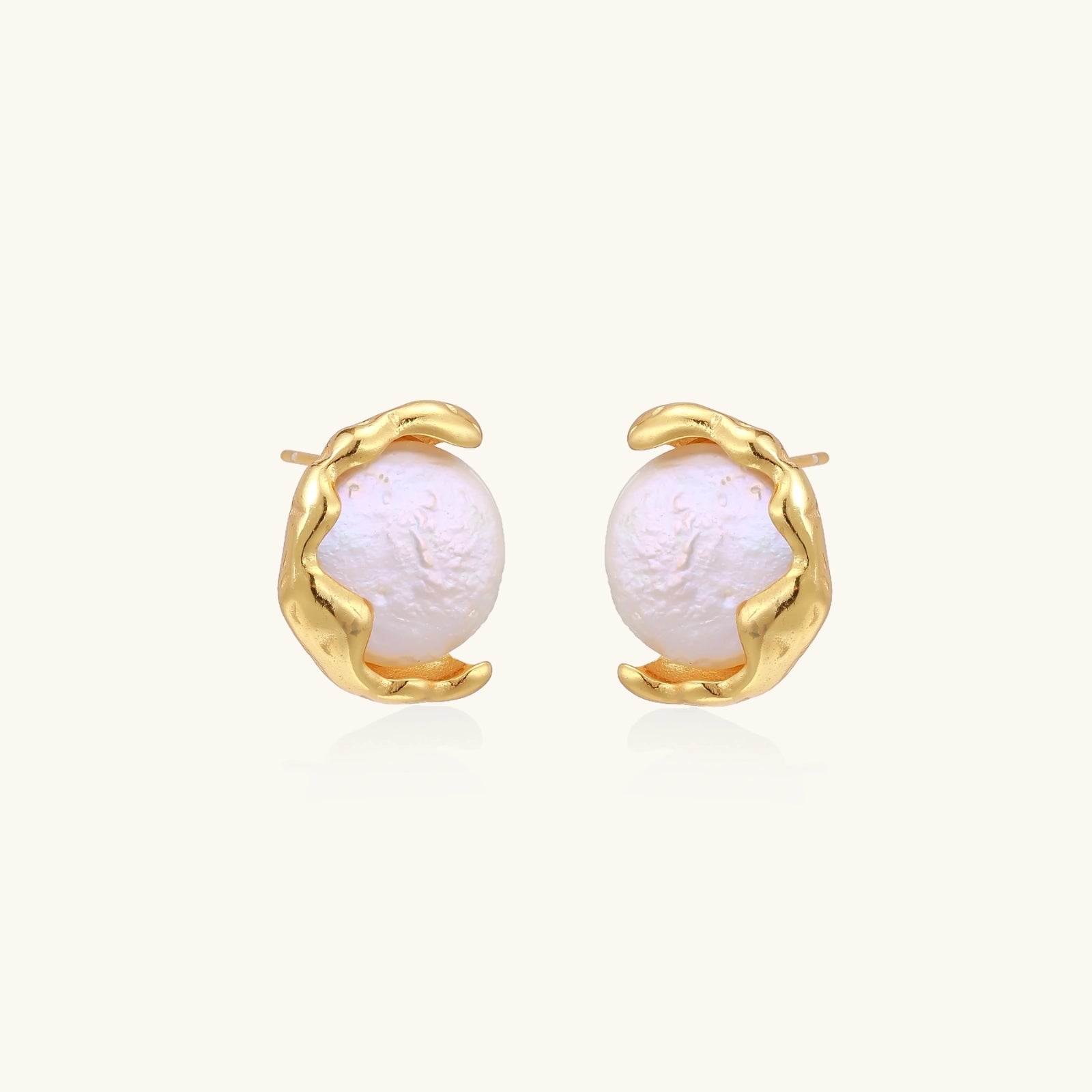 Gold earrings with pearls on a light beige background