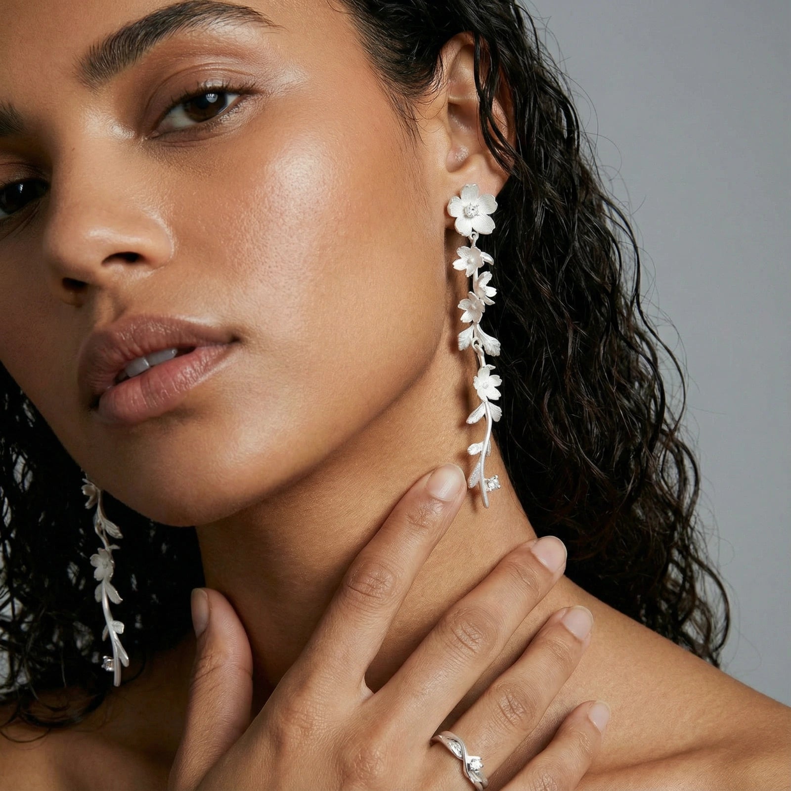 Close-up of a woman wearing silver floral earrings with a neutral background