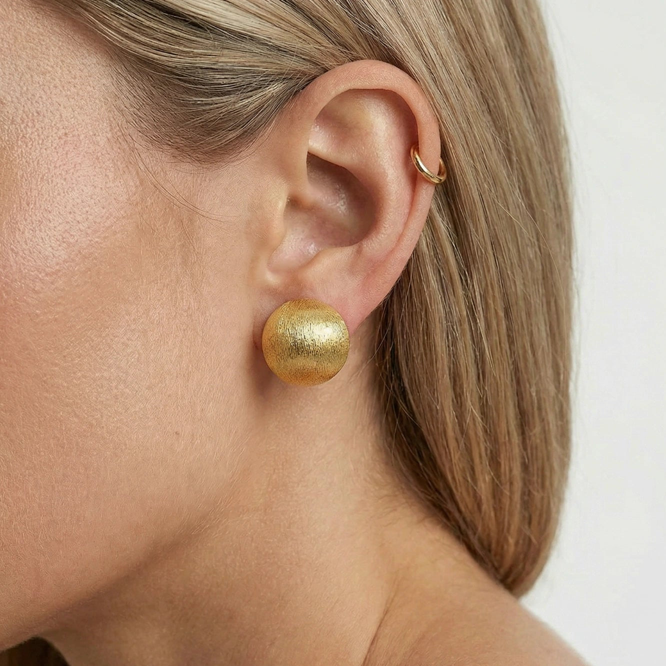 Close-up of a person wearing gold earrings with a plain background