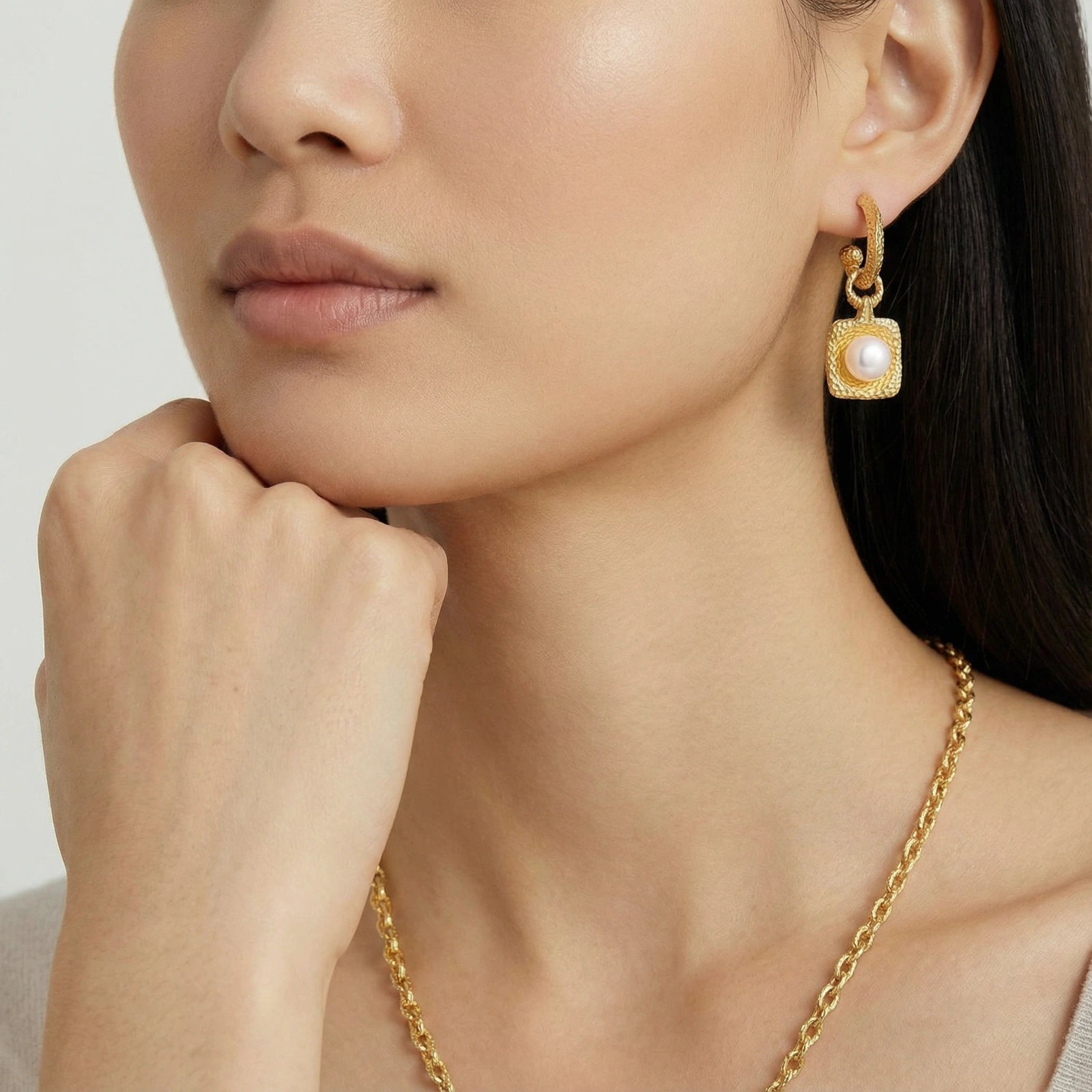 Close-up of a woman wearing gold earrings and necklace against a neutral background