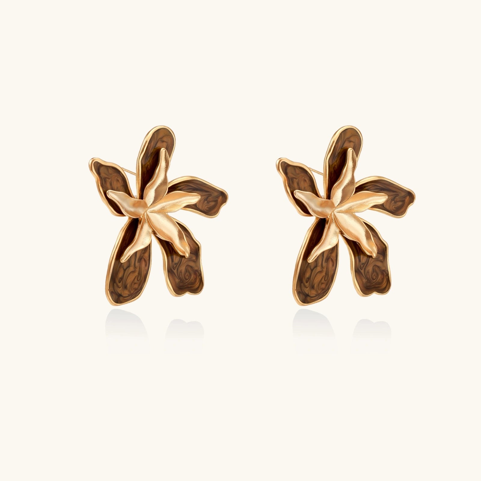 Pair of gold oragnix flower-shaped earrings on a light beige background