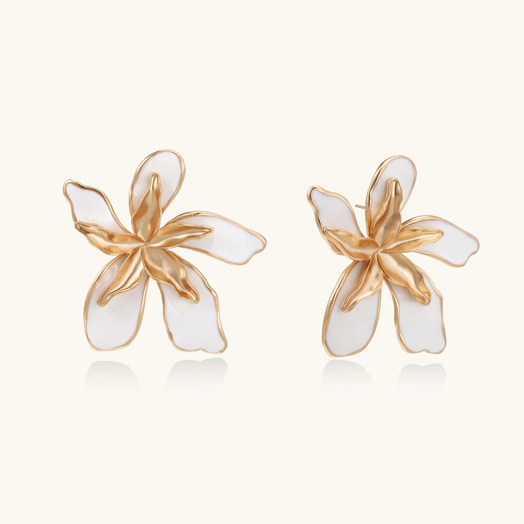 Pair of gold and white flower-shaped earrings on a light beige background
