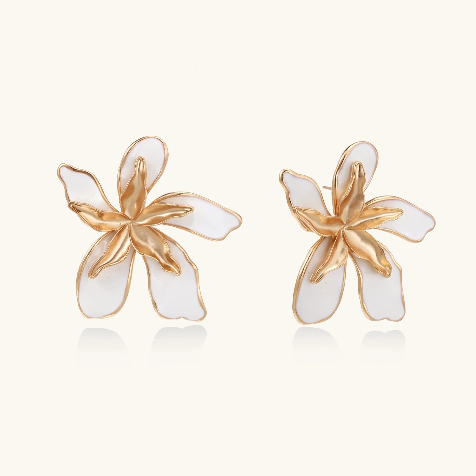 Pair of gold and white flower-shaped earrings on a light beige background