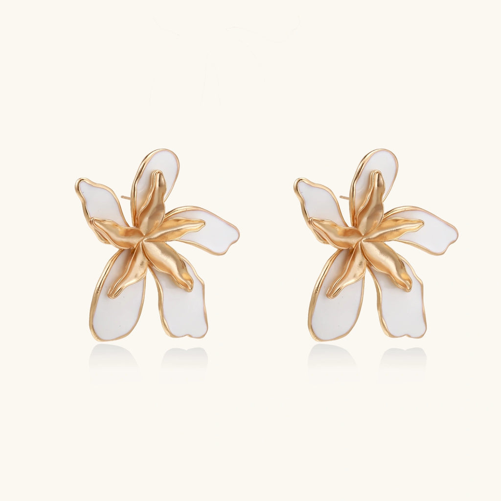 Pair of gold and white flower-shaped earrings on a light beige background