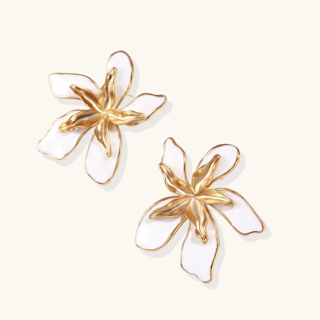 Pair of gold and white floral earrings on a light beige background