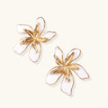 Pair of gold and white floral earrings on a light beige background