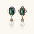 Pair of ornate earrings with gemstones and pearls on a white background