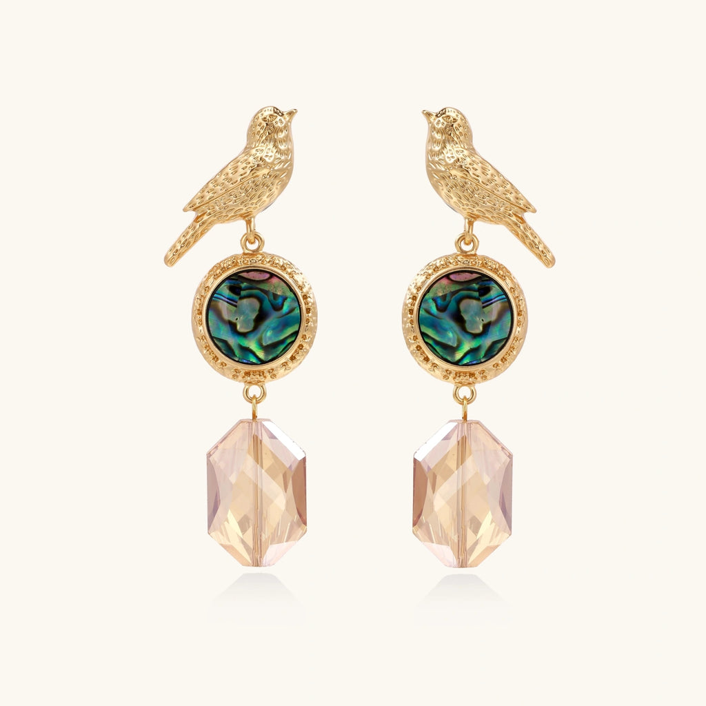 Gold bird-shaped earrings with abalone shell and crystal drop on a white background