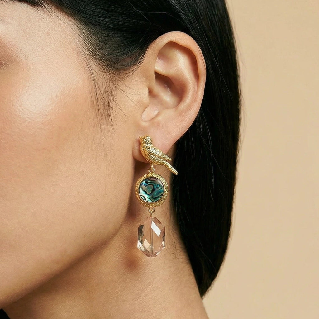 Close-up of a woman wearing a gold and green earring against a beige background