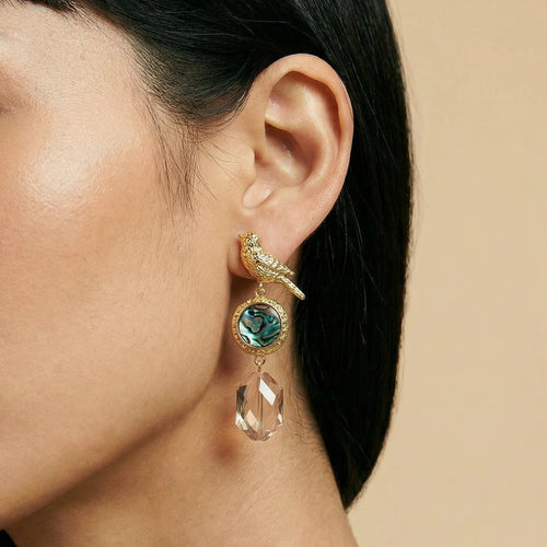 Close-up of a woman wearing a gold and green earring against a beige background