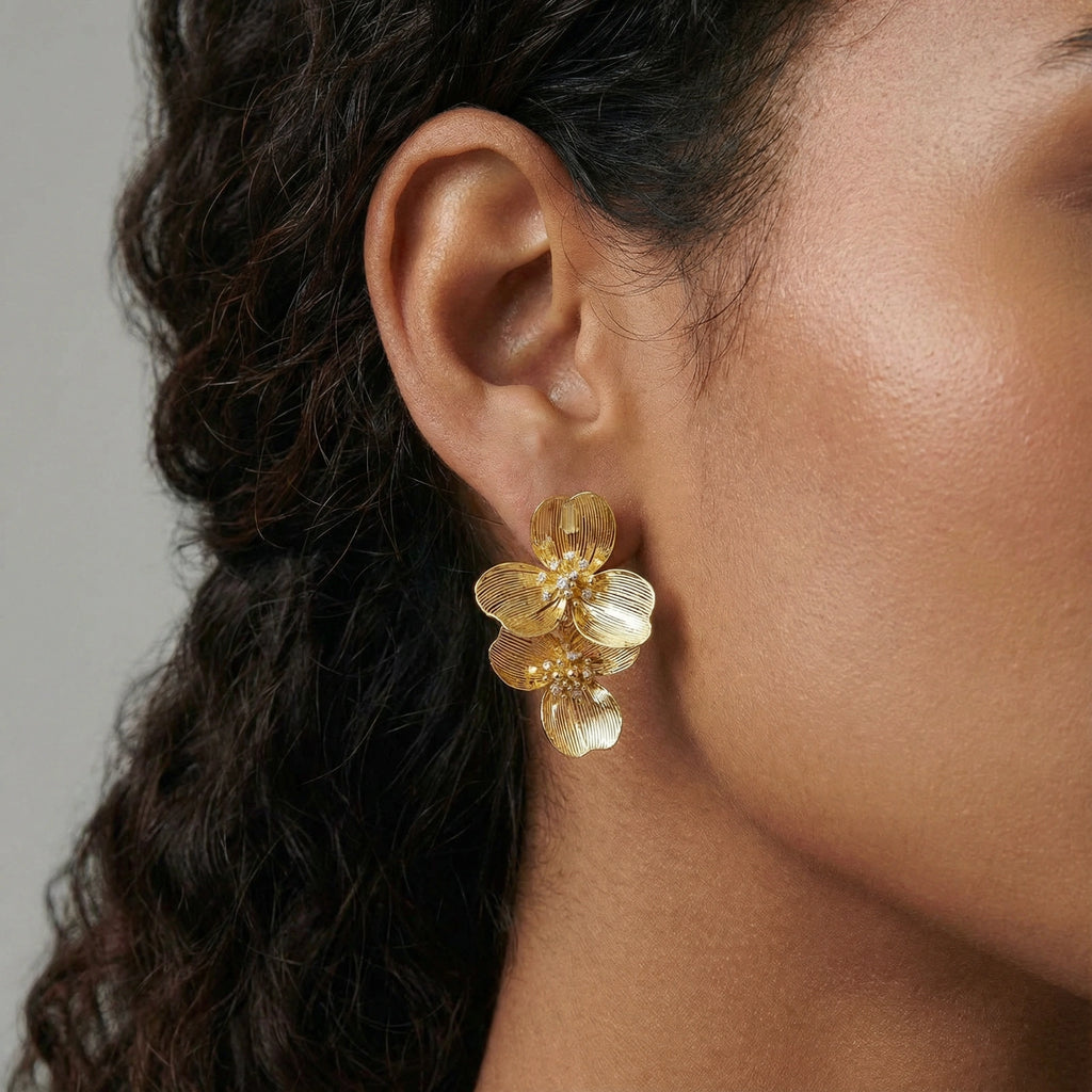 Close-up of a person wearing gold floral earrings with a neutral background
