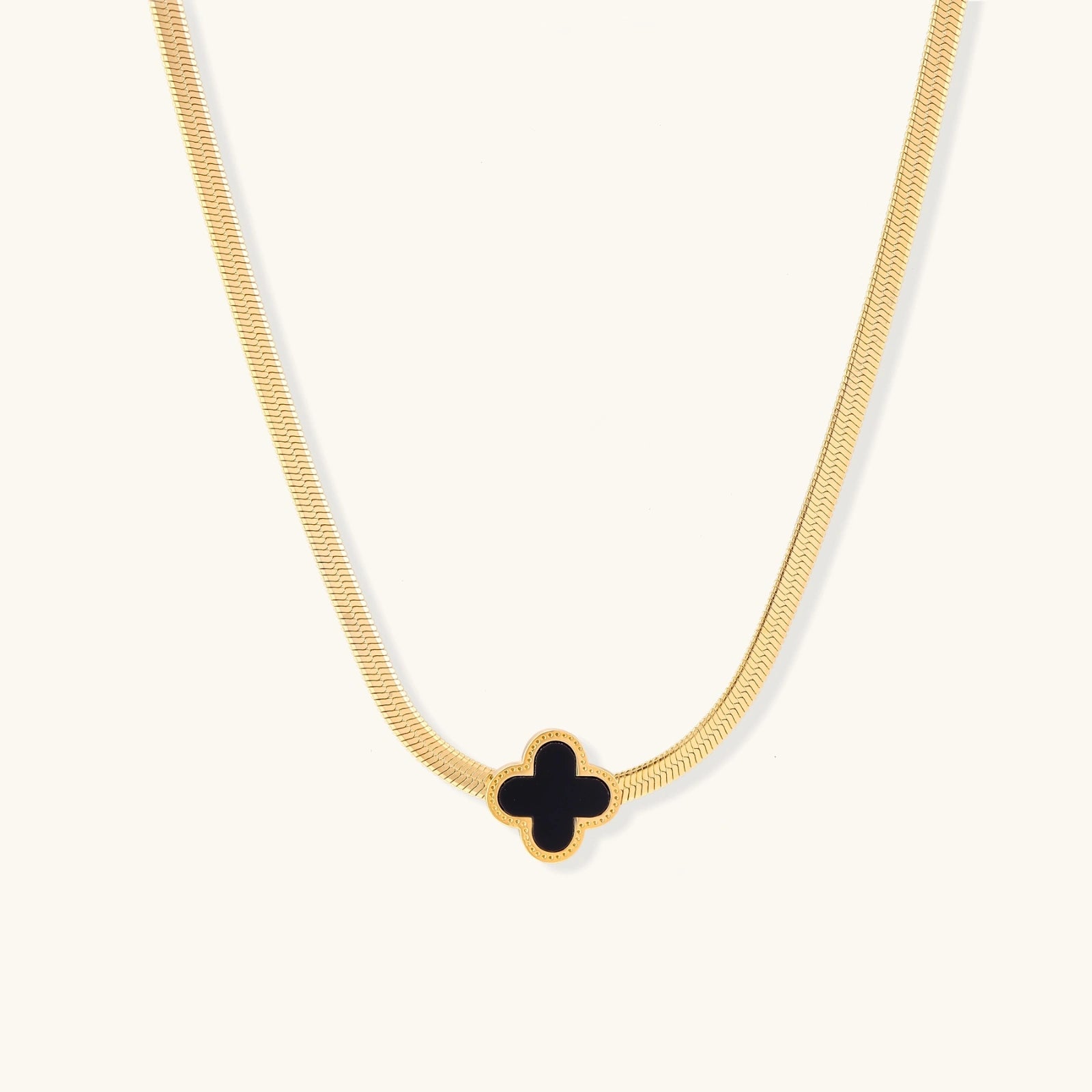 Gold necklace with a black clover-shaped pendant on a white background