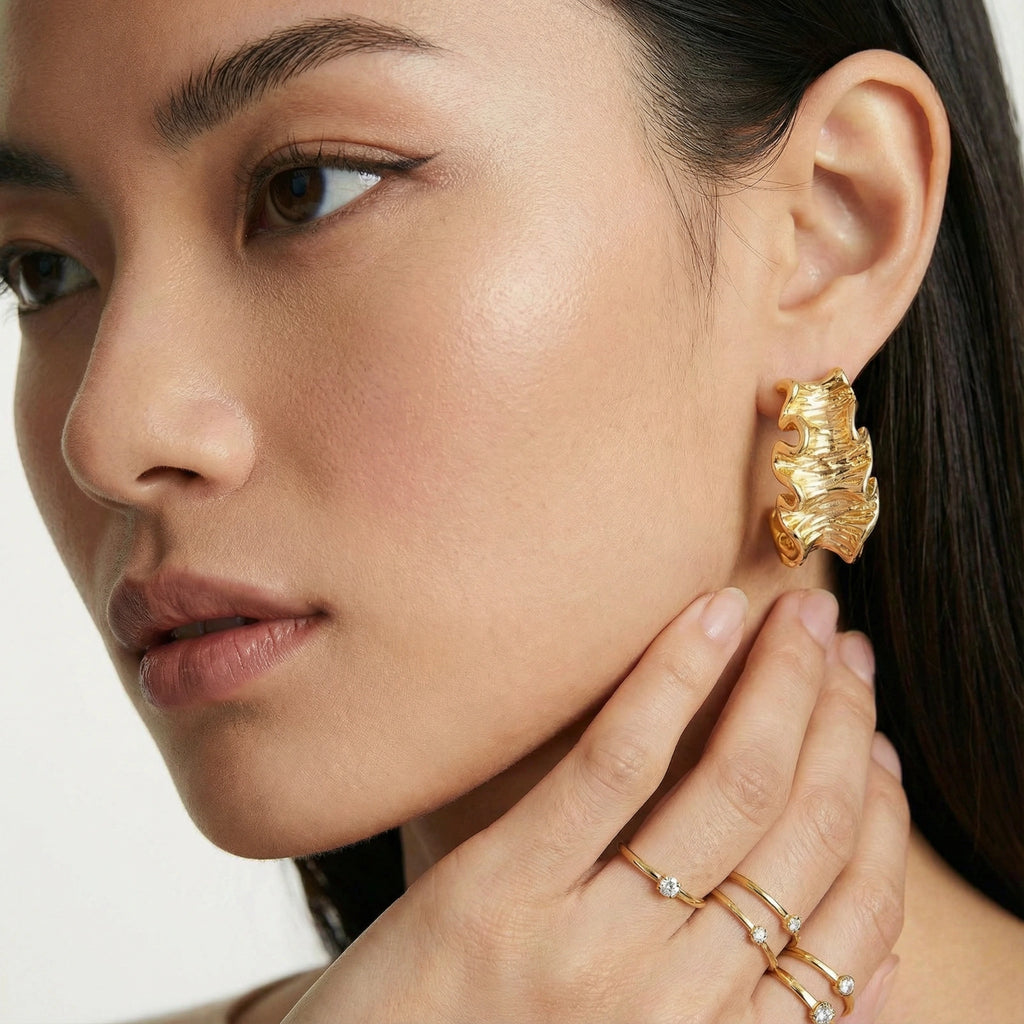 Close-up of a woman wearing gold earrings and rings on a white background