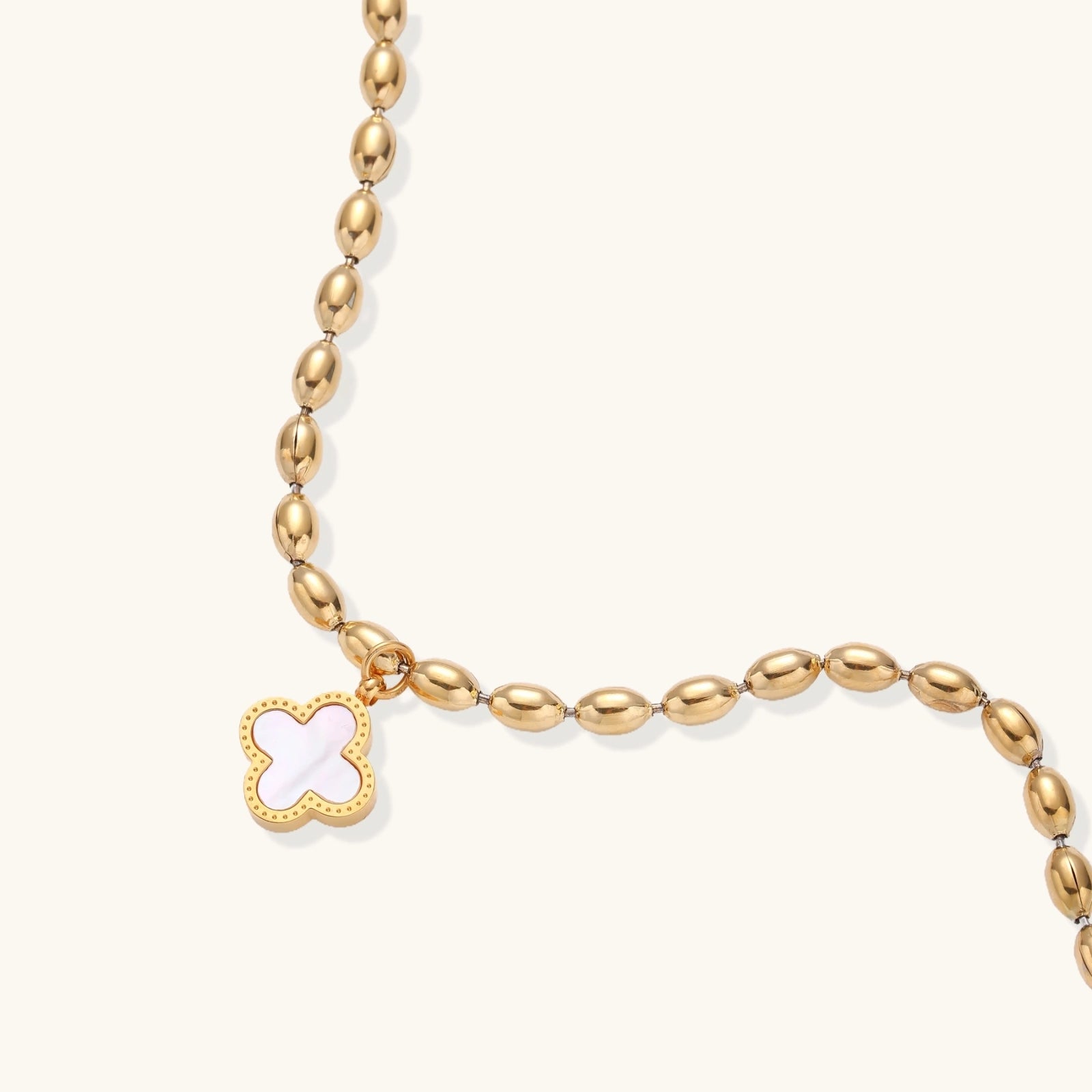 Gold beaded bracelet with a clover-shaped charm on a white background