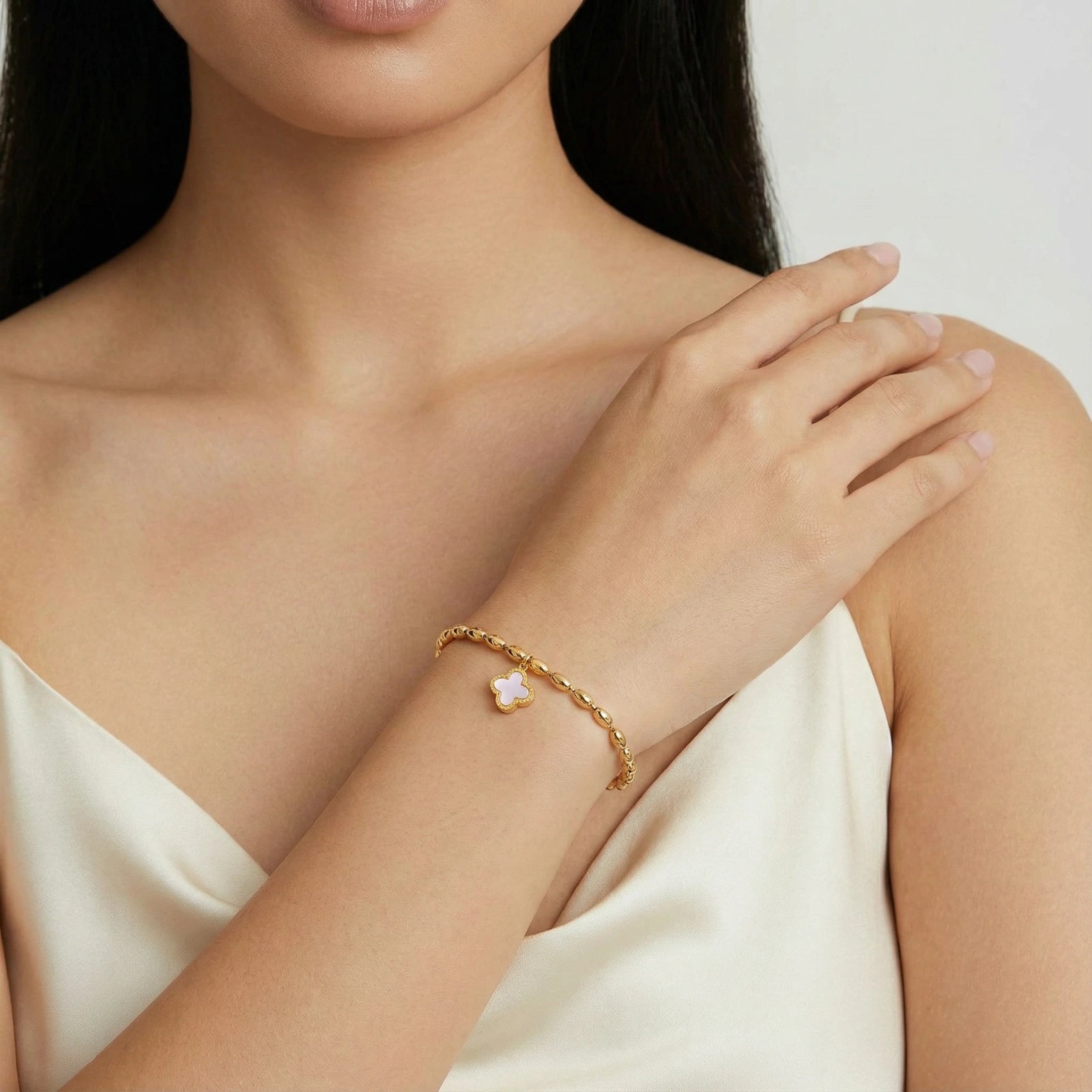 Close-up of a woman's arm wearing a gold bracelet with a heart charm on a neutral background