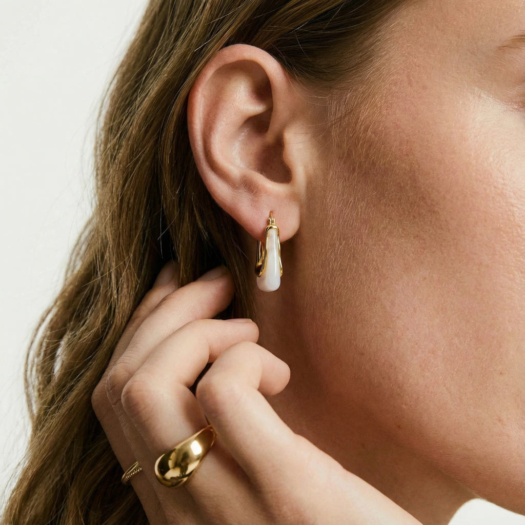 Close-up of a person wearing a gold earring and ring on a neutral background
