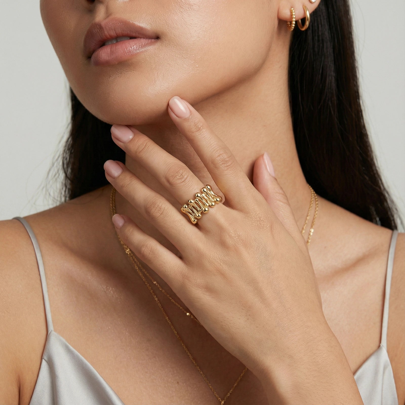 Close-up of a woman wearing gold jewelry including a ring, necklace, and earrings.