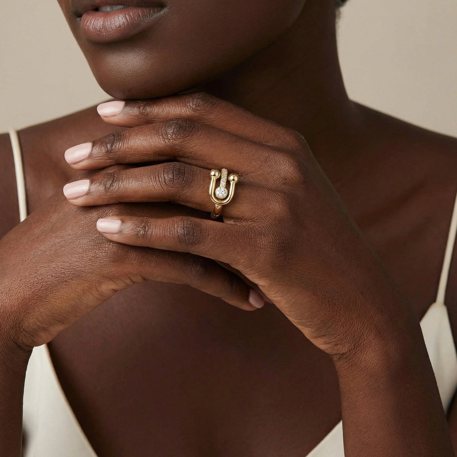 Close-up of a hand wearing a gold ring with a diamond on a neutral background