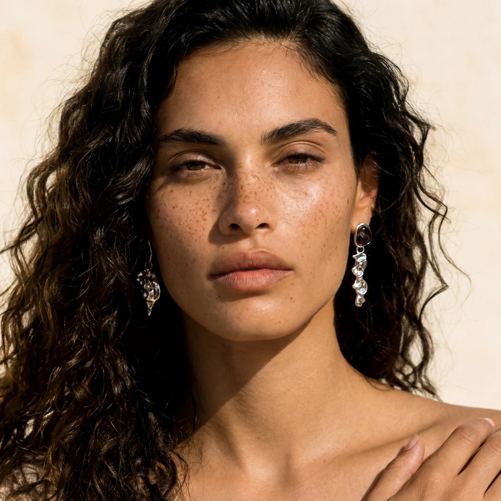 Woman with curly hair wearing earrings against a neutral background