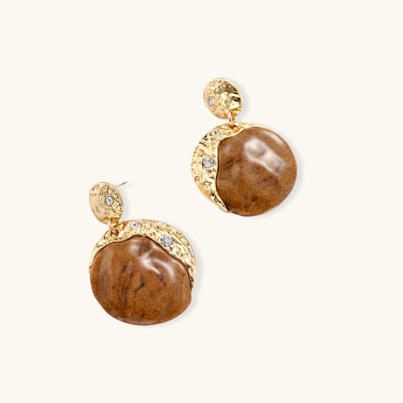 Pair of earrings with gold hammered and wooden design with rhinestones on a white background