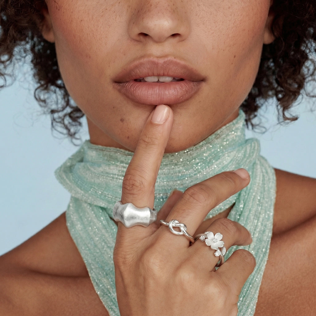 Close-up of a woman's hand with silver rings, wearing a light green scarf against a blue background