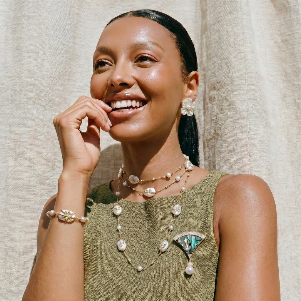 Woman wearing a green dress with pearl embellishments and pearl pin against a neutral background