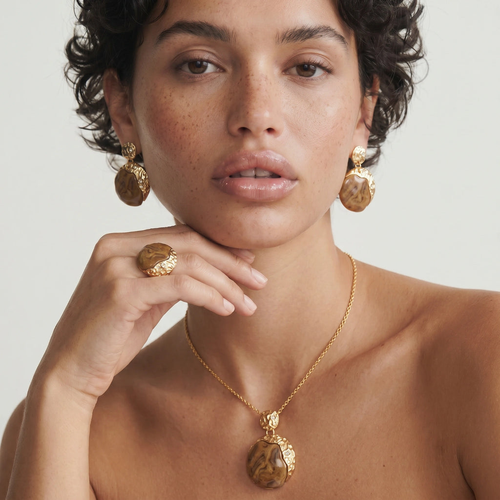Woman wearing gold jewelry including earrings, necklace, and ring on a plain background