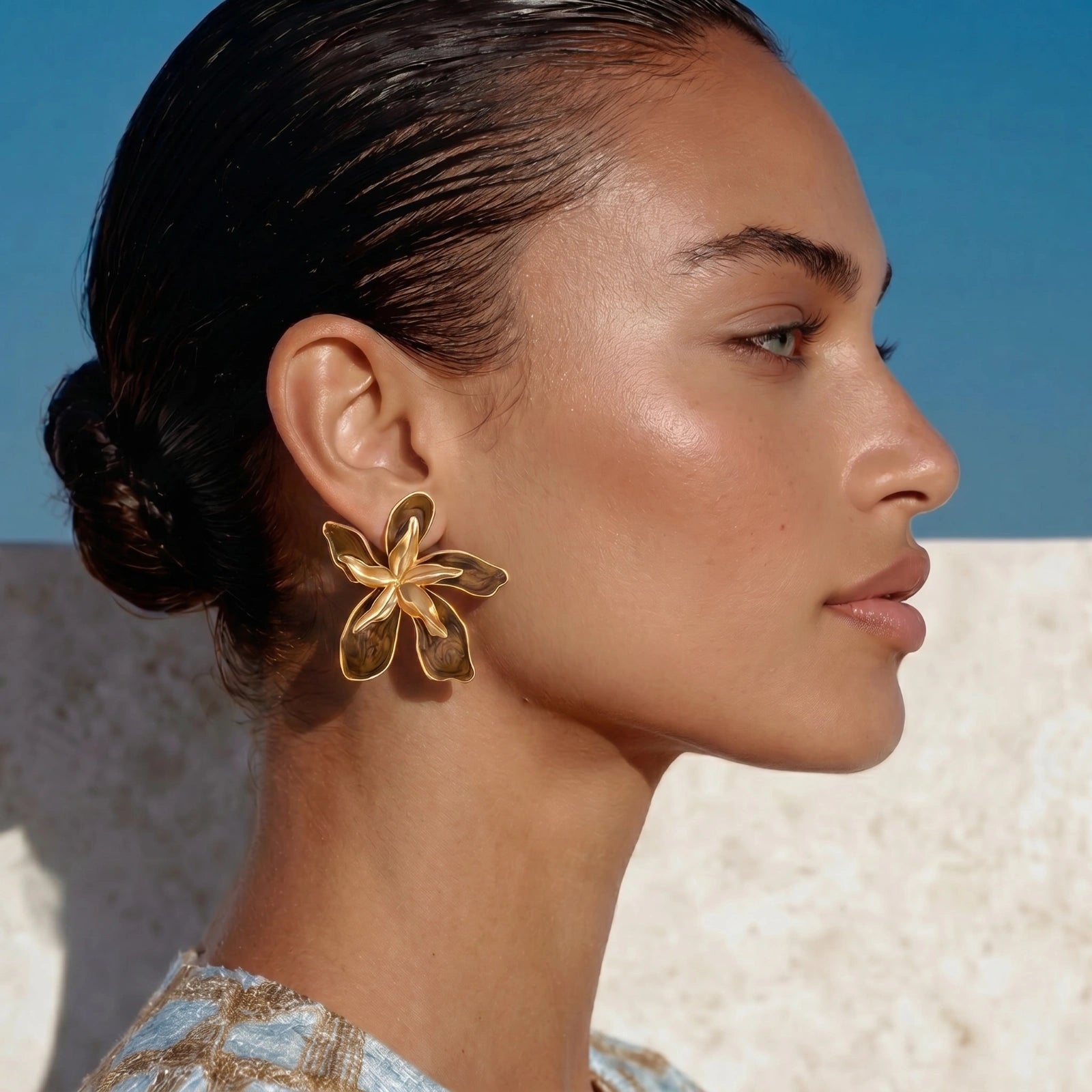 Woman wearing a gold flower earring with a clear blue sky background