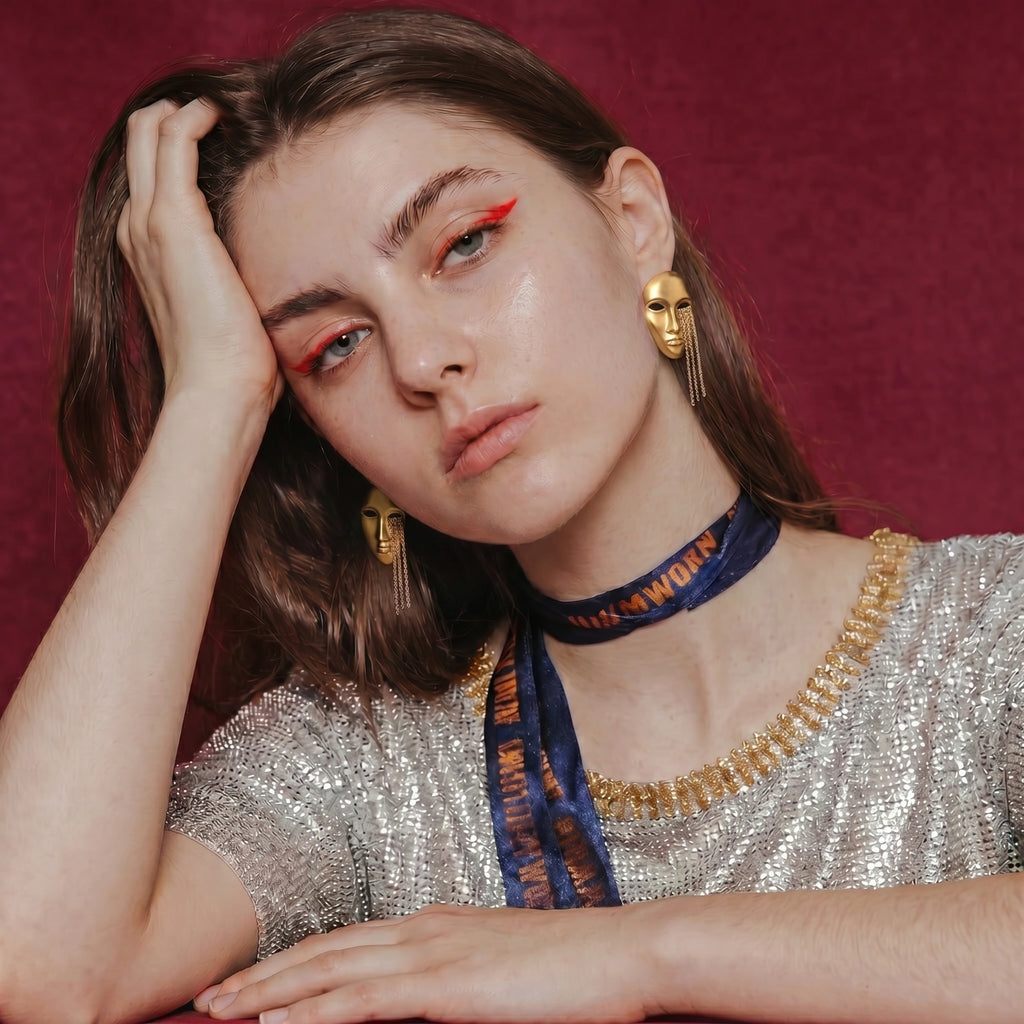 Woman wearing gold face earrings and a silver top with a red background
