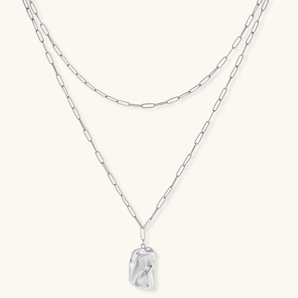 Layered silver chain necklaces with a clear crystal pendant on a white background