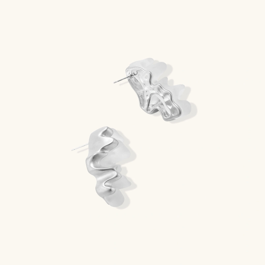 Pair of white spiral hoop earrings on a light beige background
