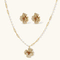 Gold floral necklace and earrings with pearl accents on a white background