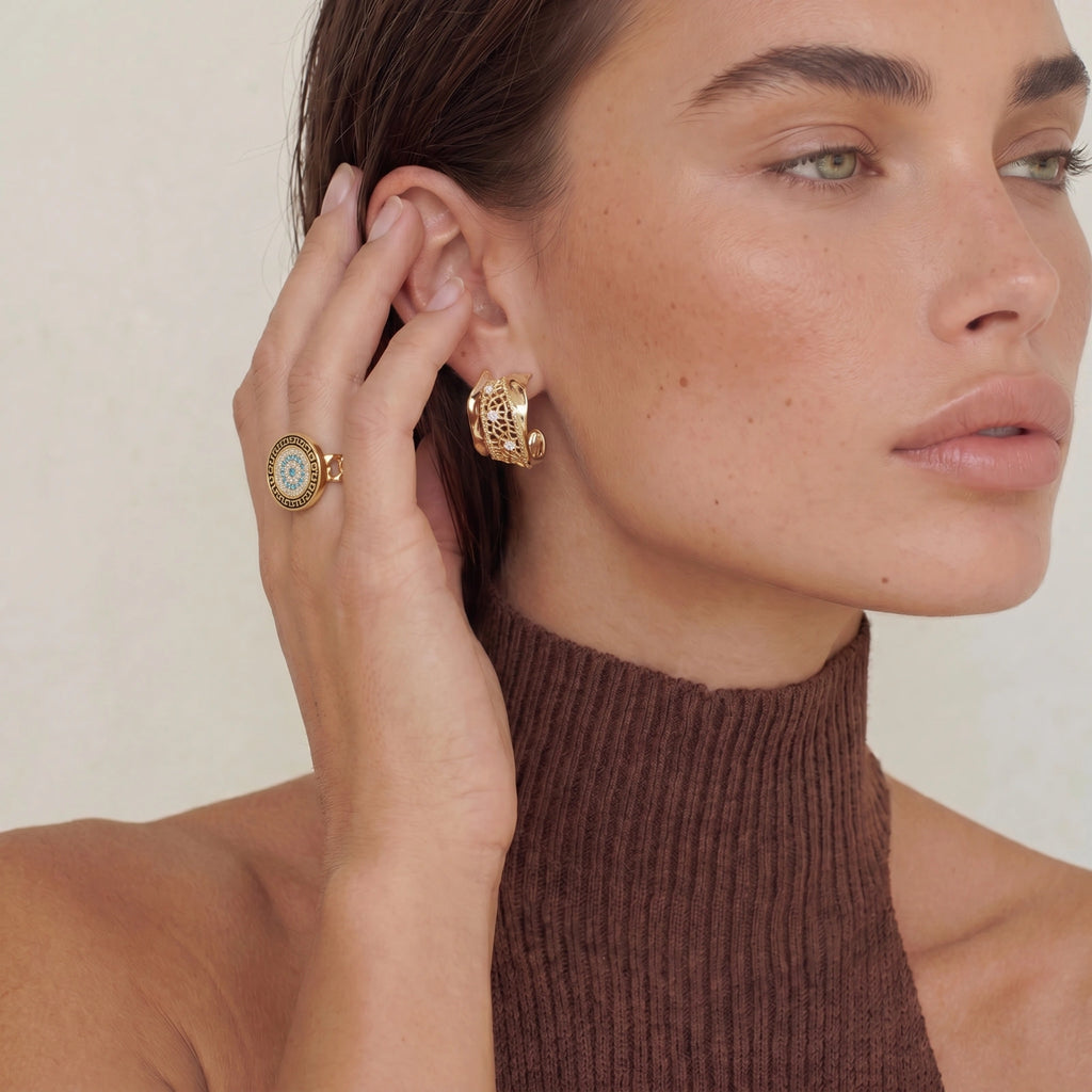 Woman wearing gold hoop earrings and a ring, with a neutral background